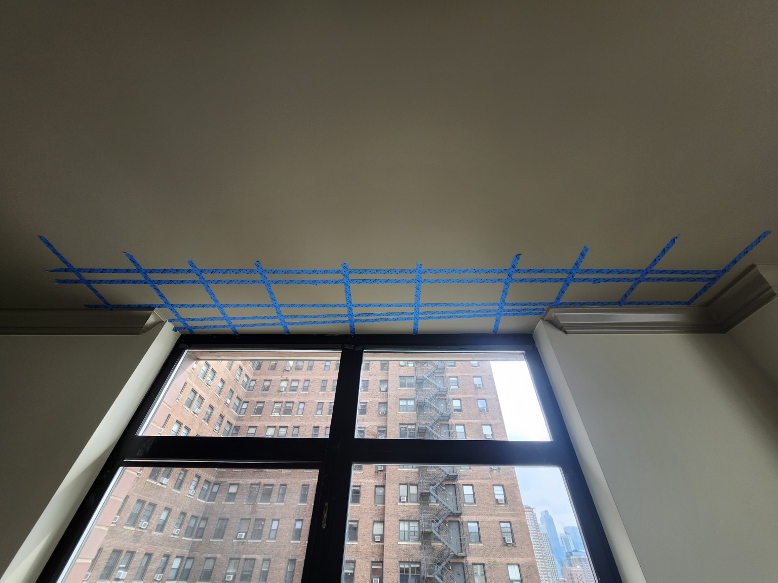 A painted ceiling above a large window, marked with a grid of blue painter's tape lines.
