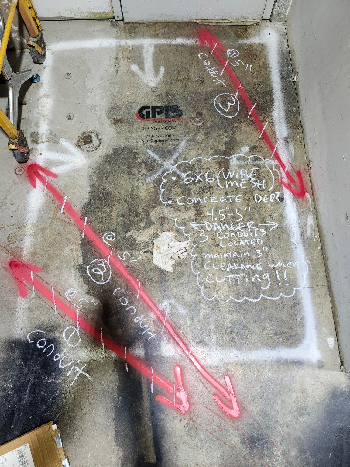 A concrete floor marked for cutting: a white rectangle outlines the cut area, three pink spray-painted conduit lines cross it, and chalk notes read 6x6 wire mesh, concrete depth 4.5 to 5 inches, danger, three conduits located, maintain 3 inch clearance when cutting. A GPIS stencil is painted on the slab.