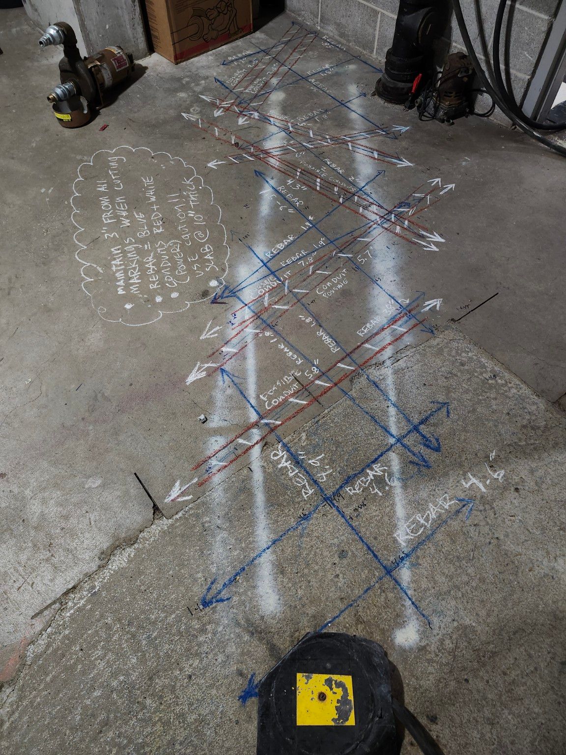 A basement slab covered in a dense grid of blue rebar lines and red and white conduit lines, each labeled with a depth, with a chalk note: maintain 3 inches from all markings when cutting, rebar blue, conduits red and white, slab 10 inches thick.